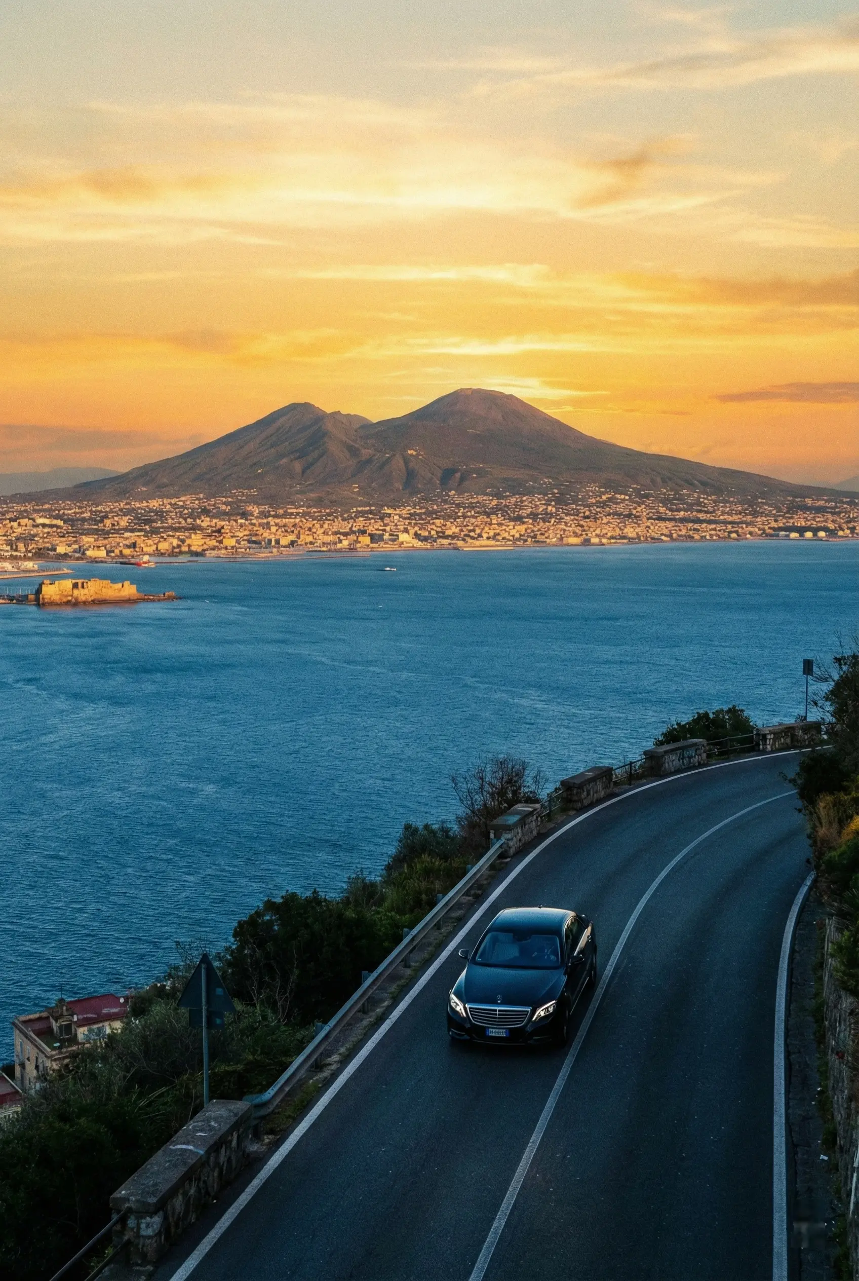 Mount Vesuvius view during private transfer Rome to Amalfi Coast A luxury Mercedes private transfer car driving along the scenic coastal road at sunset, with Mount Vesuvius dominating the Bay of Naples background during the journey from Rome to the Amalfi Coast.