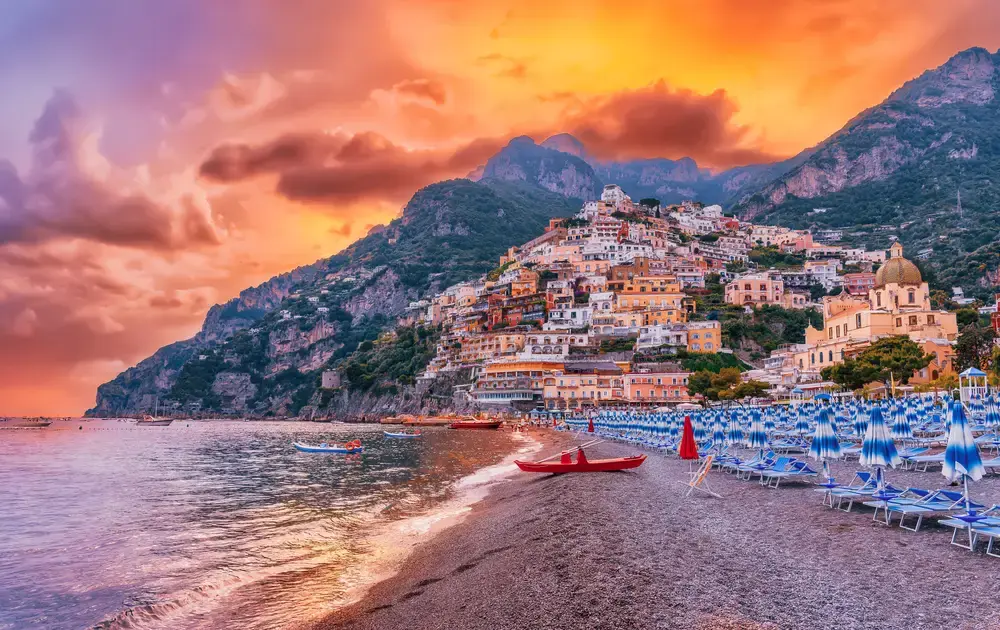 positano view The colorful vertical village of Positano on the Amalfi Coast at sunset, showing the winding roads and cliffside houses. A top destination for luxury private transfers.