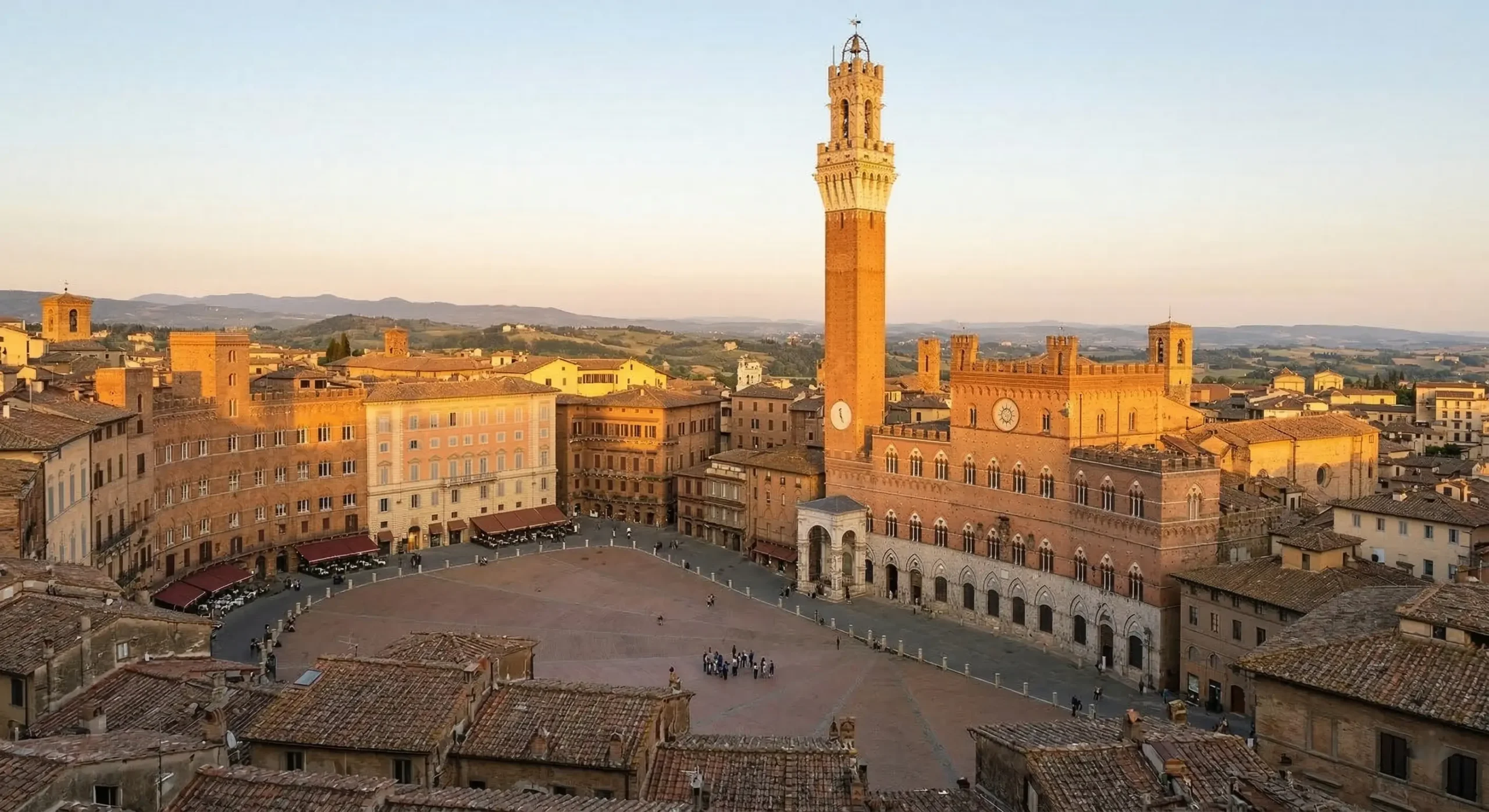 Siena shells-shaped Piazza del Campo and Torre del Mangia with surrounding medieval architecture under warm golden hour light.